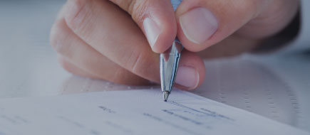 up close photo of a hand holding a pen and signing a check