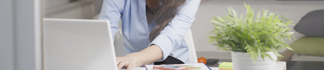 photo image of lady typing on a computer at a desk, with a green plant in a white container on the left side of her 