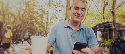 photo of an older man drinking coffee while sitting in a park and working on his mobile phone.