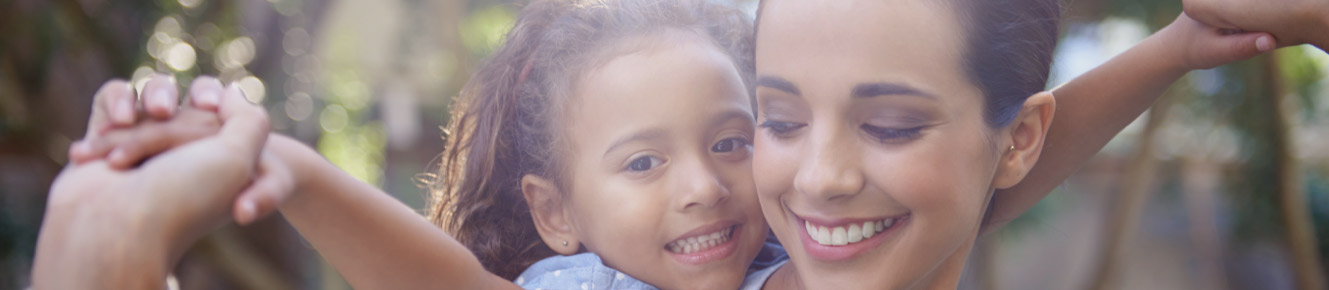 photo of little girl leaning over a lady's shoulder holding their hands together up in the air and smiling  